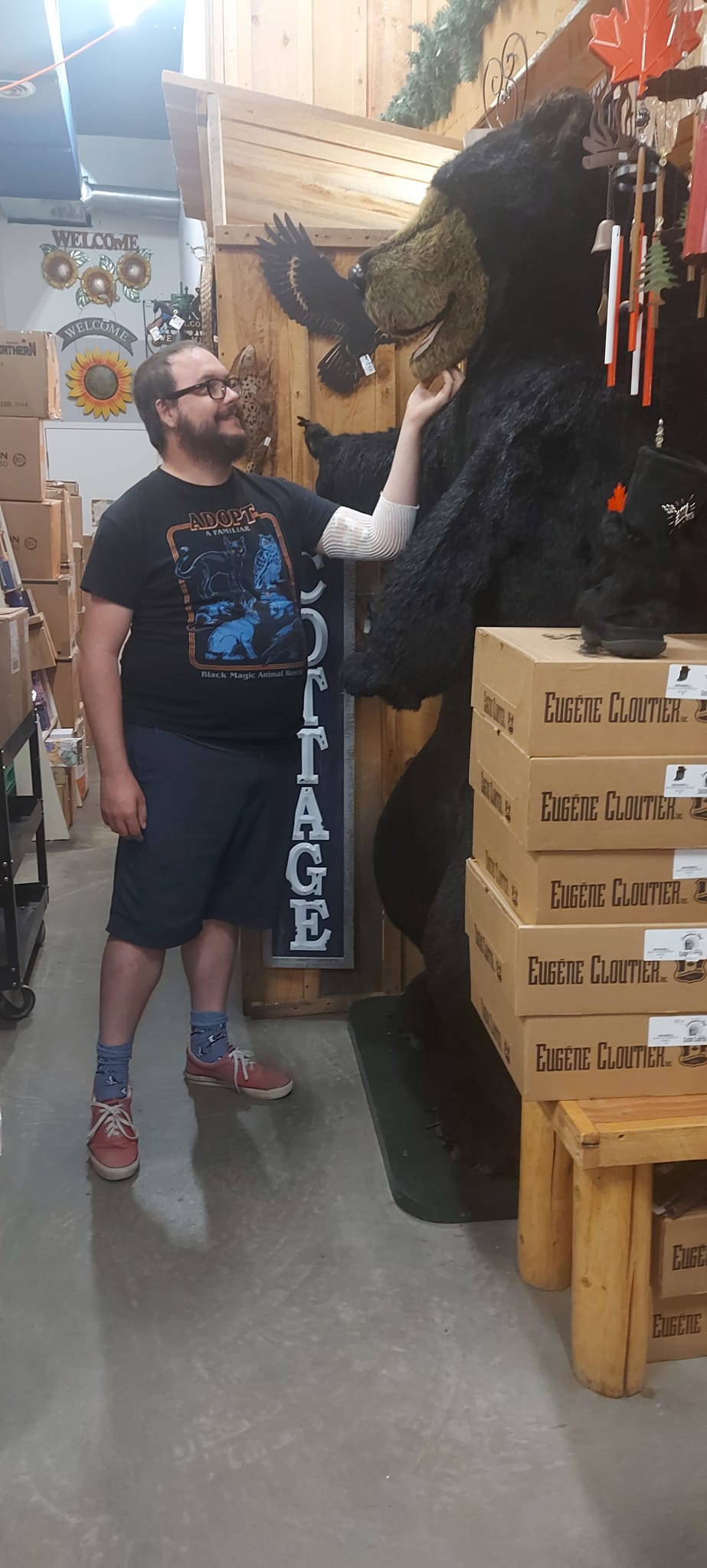 A man short hair and bushy facial hair scratches the chin of a large fluffy black bear statue